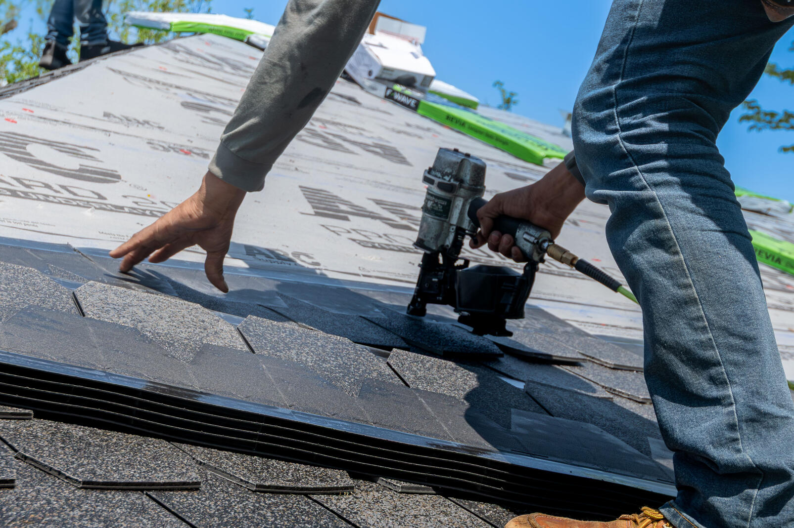 someone using a nail gun to nail roofing shingles